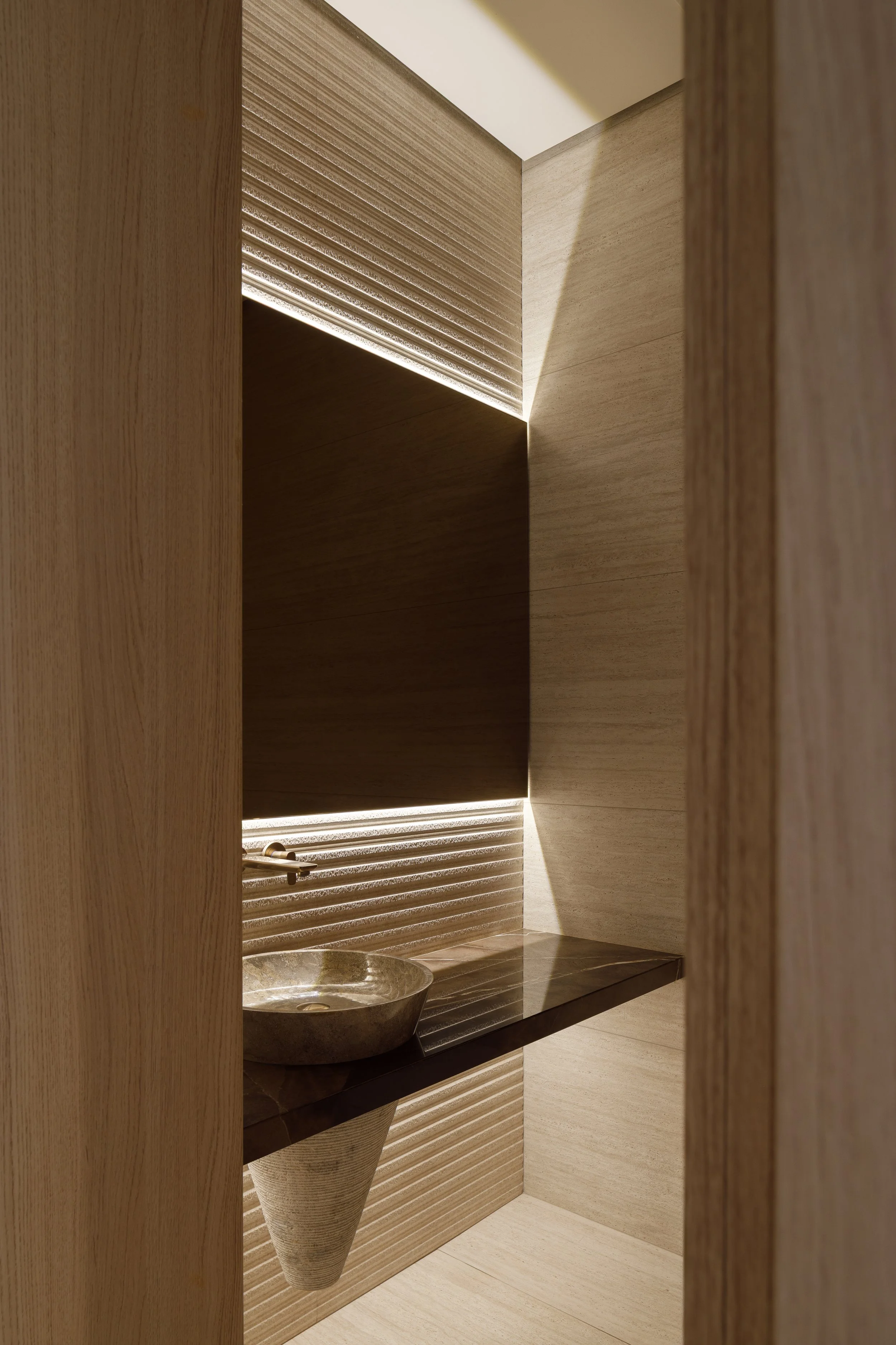 Detalle de lavabo con encimera veteada y revestimiento en tonos beige.