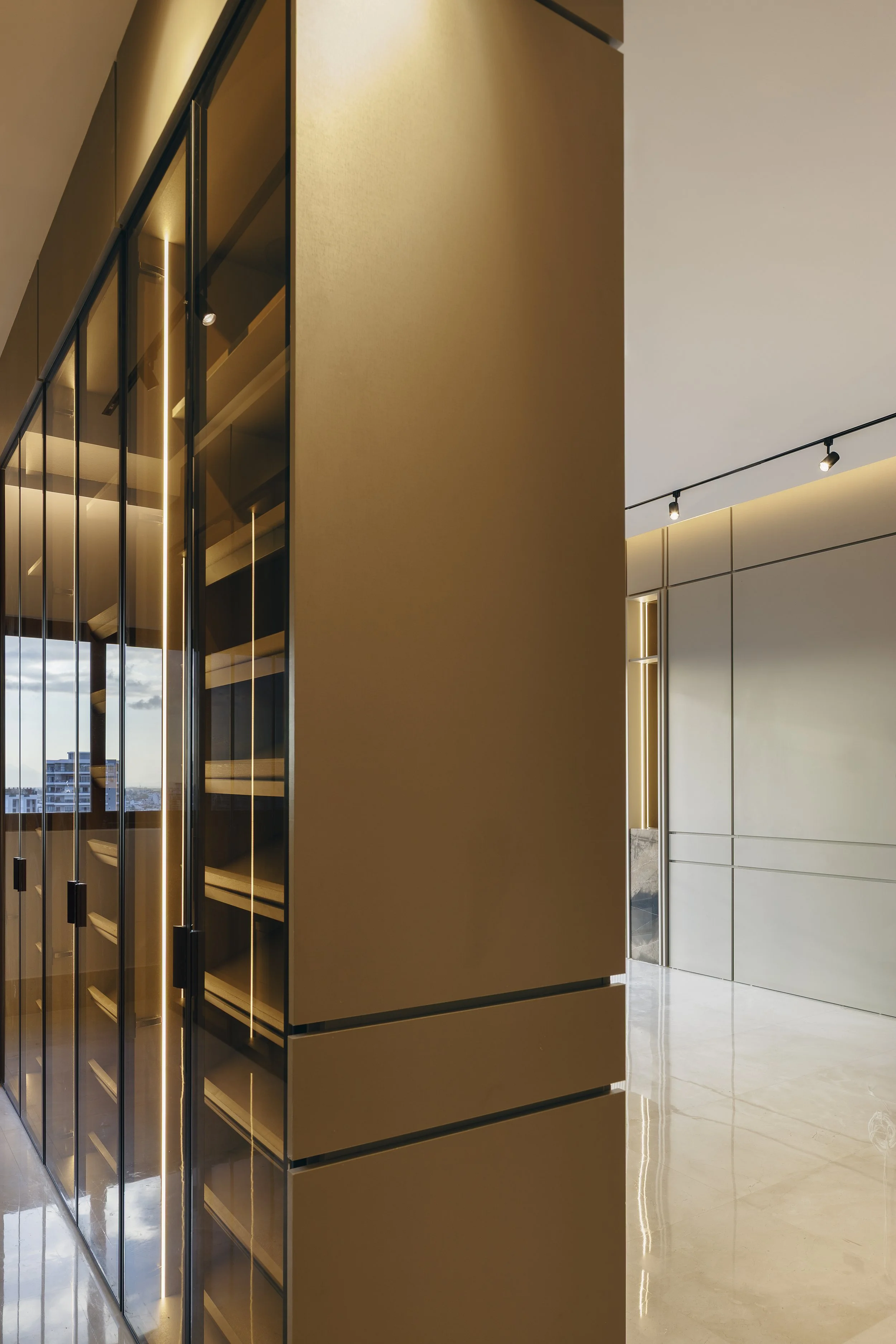 Interiores modernos con paredes beige, ventanas de piso a techo con marcos negros, iluminación en el techo, pisos de mármol claro y mobiliario minimalista.