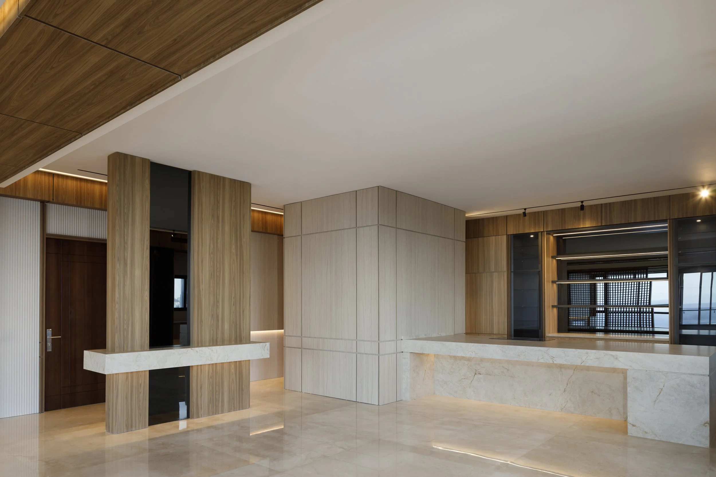 Interior de un edificio moderno con paredes y columnas de madera clara y detalles de mármol en el suelo y en una esquina.