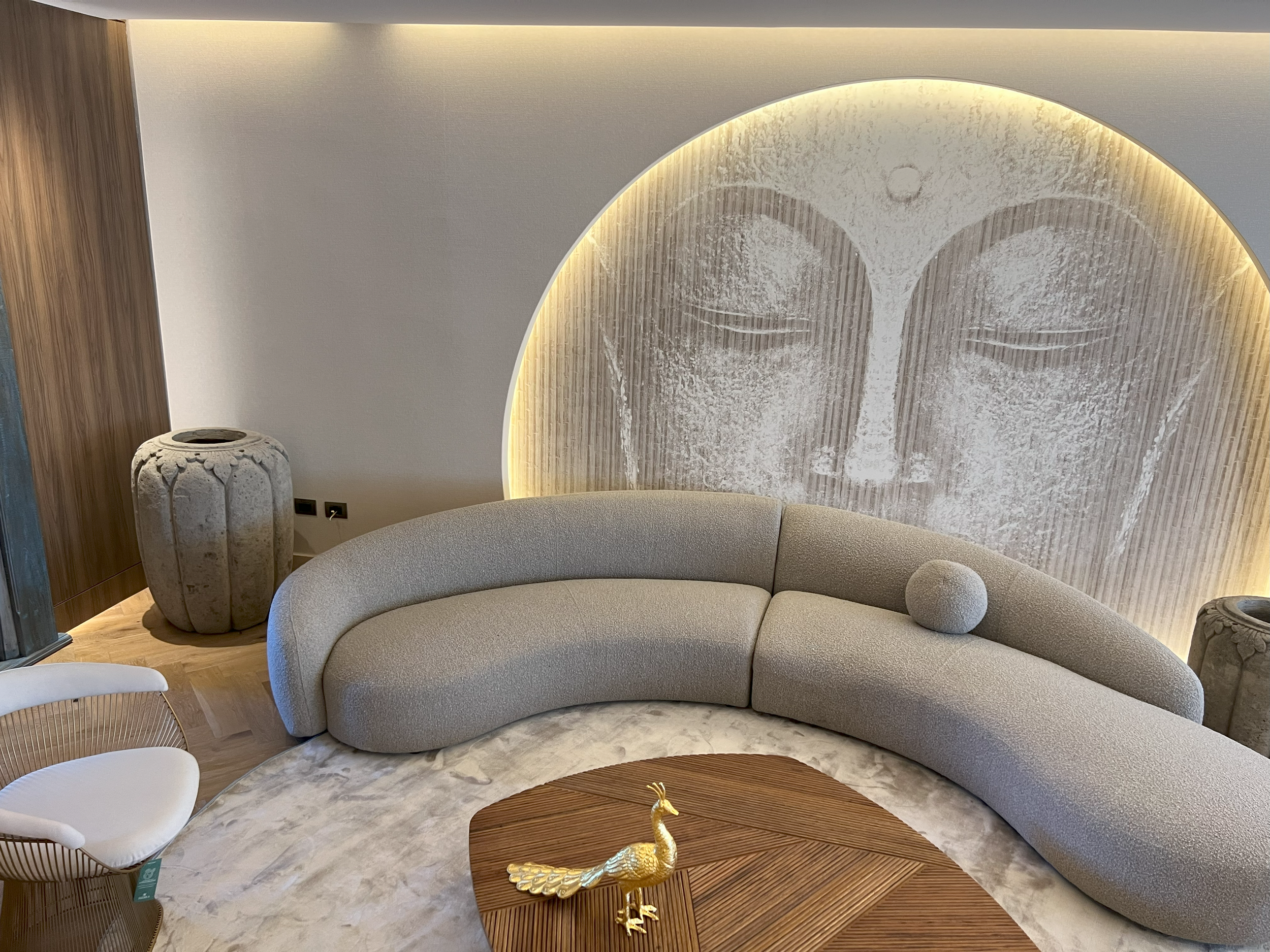 Sala de estar con sofá curvo claro, mesa de centro de madera y mural circular iluminado.