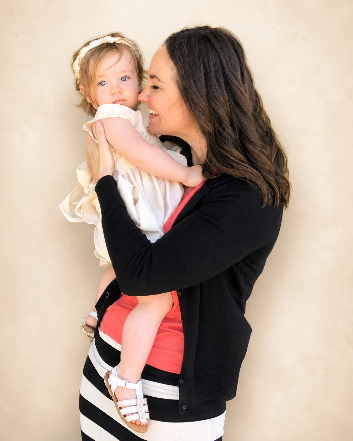 Ava holding her young daughter close against a soft cream background, sharing a warm, affectionate moment.