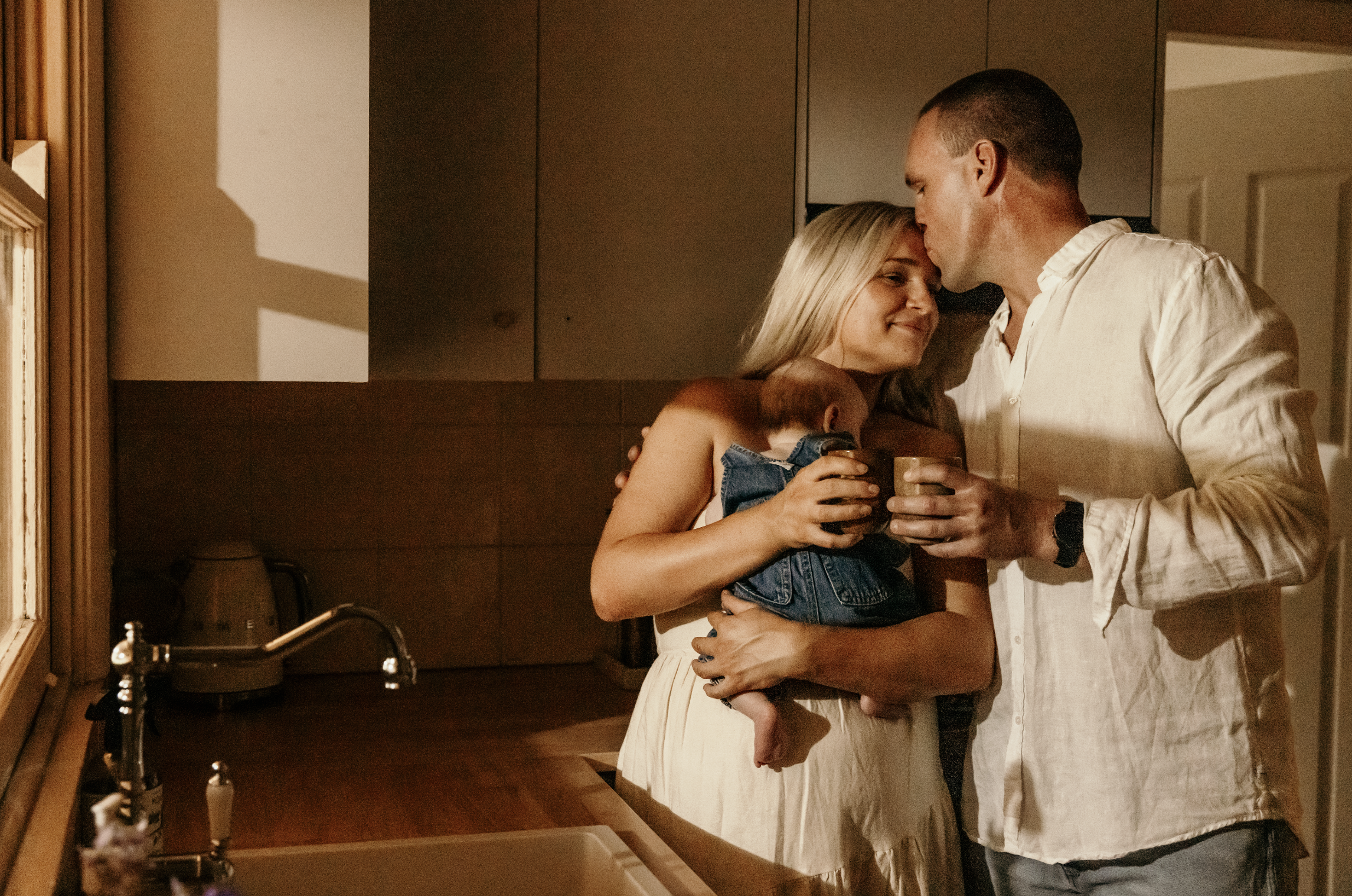 A couple holding their baby in a cozy kitchen, sharing a moment with warm lighting.