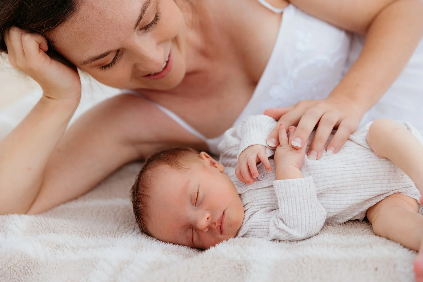 A woman and a baby sleeping on a soft, cream-colored blanket.