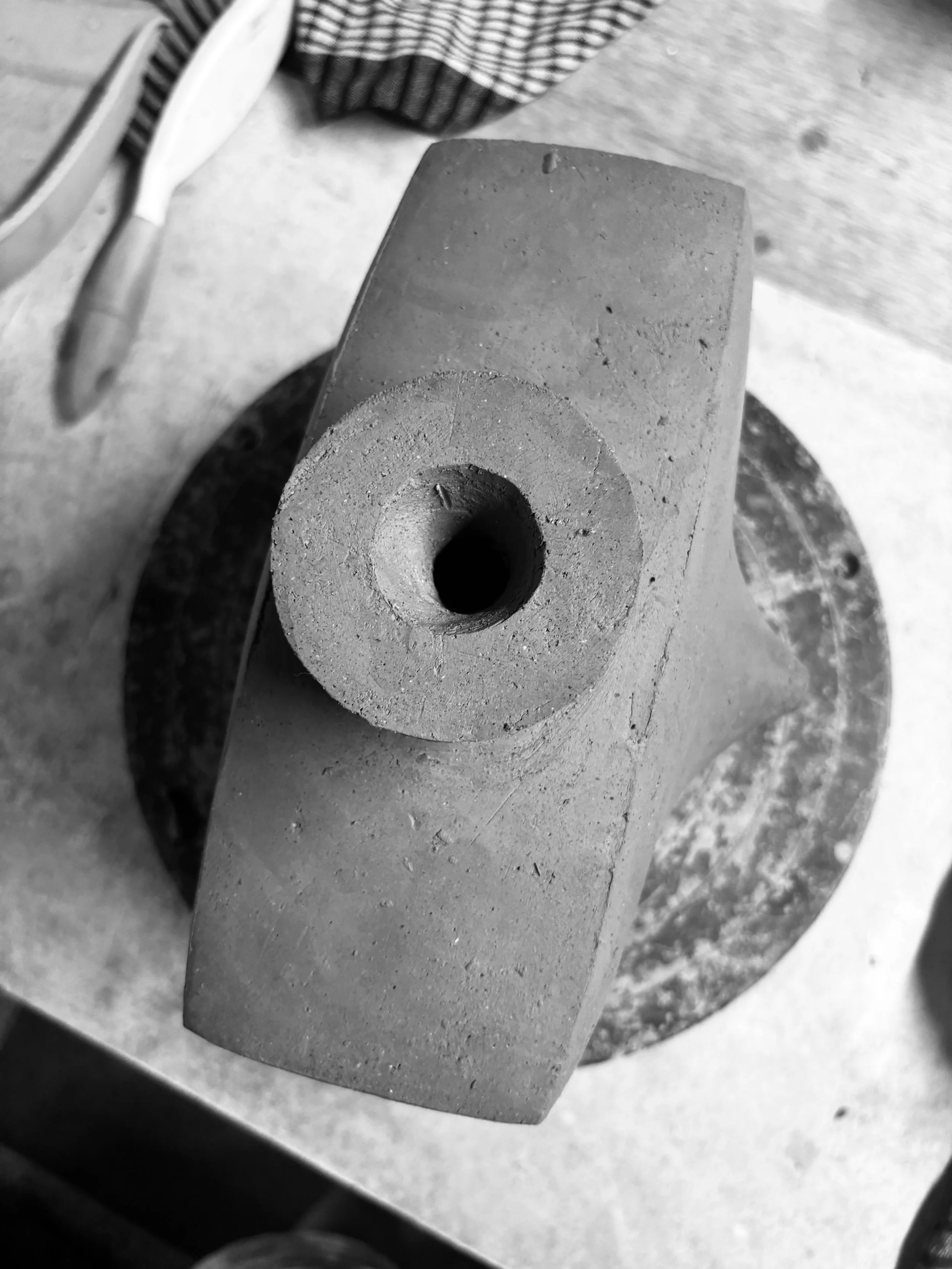 Close-up of a cylindrical clay object with a hollow center on a round, flat surface.