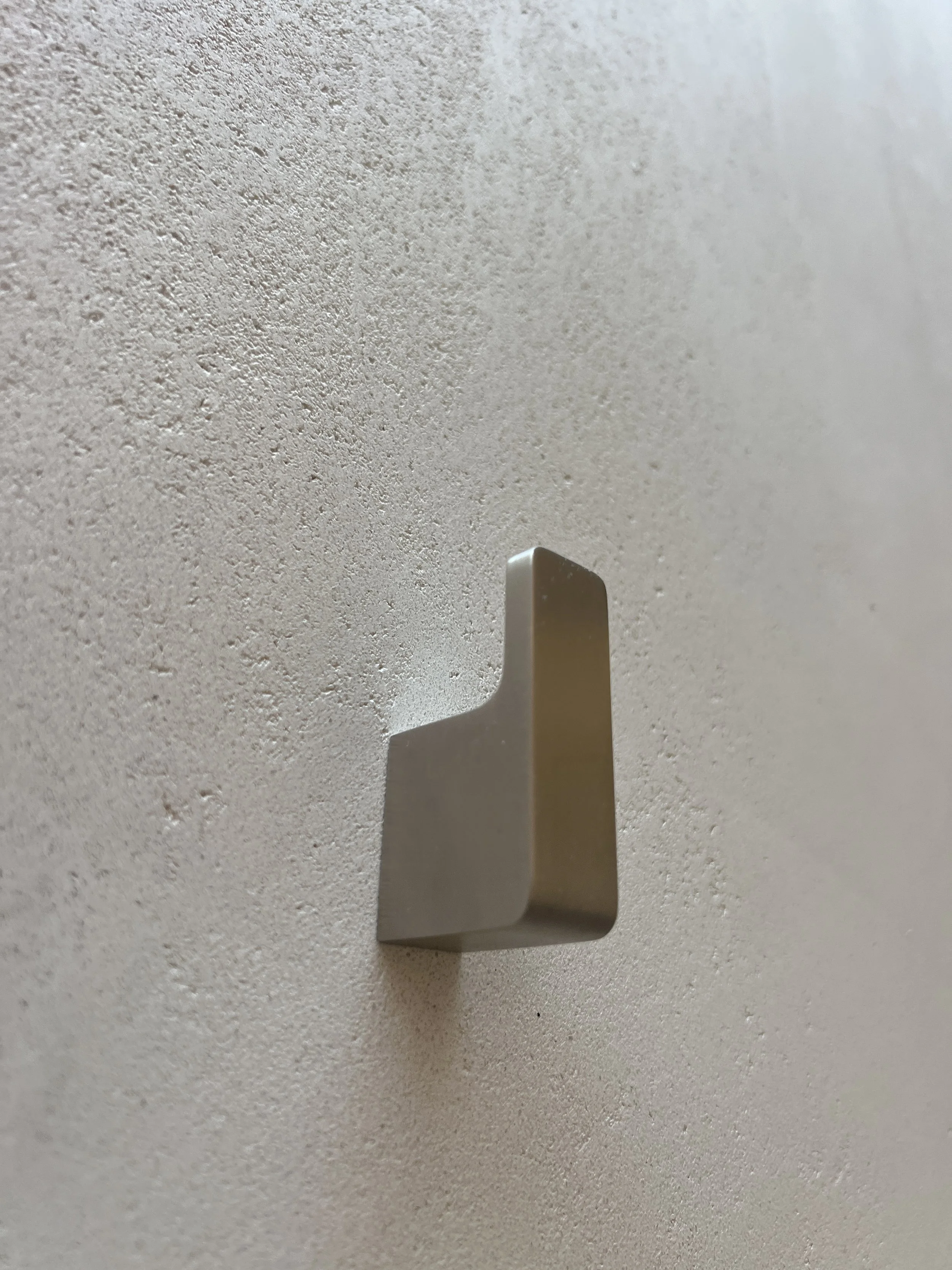 Close-up view of a beige plastic hook attached to a textured white wall.