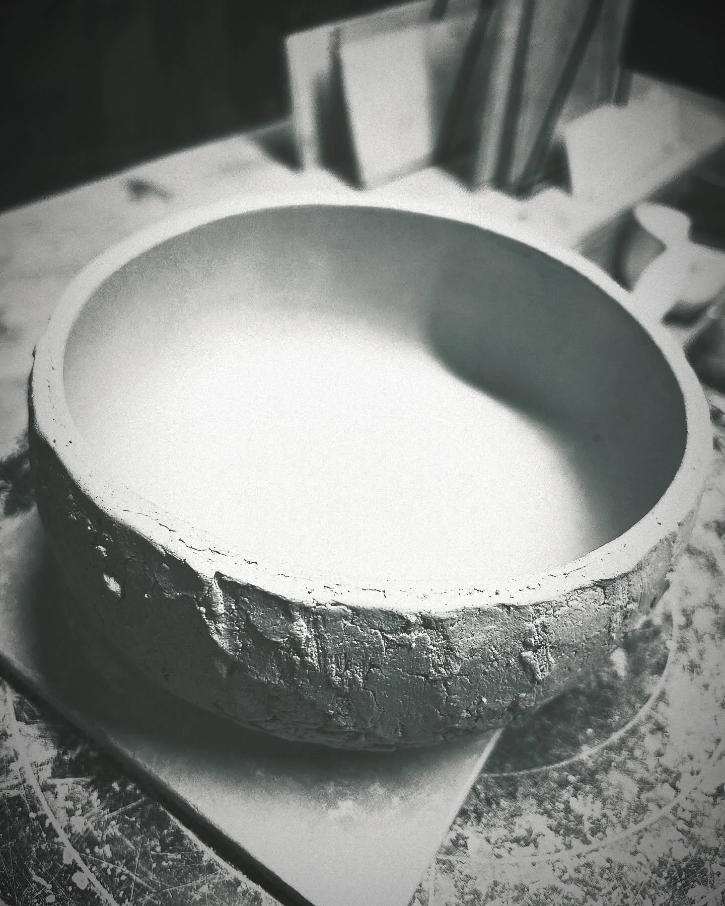 A round ceramic bowl with a textured exterior, filled with a white substance, placed on a work surface with art supplies and books in the background.