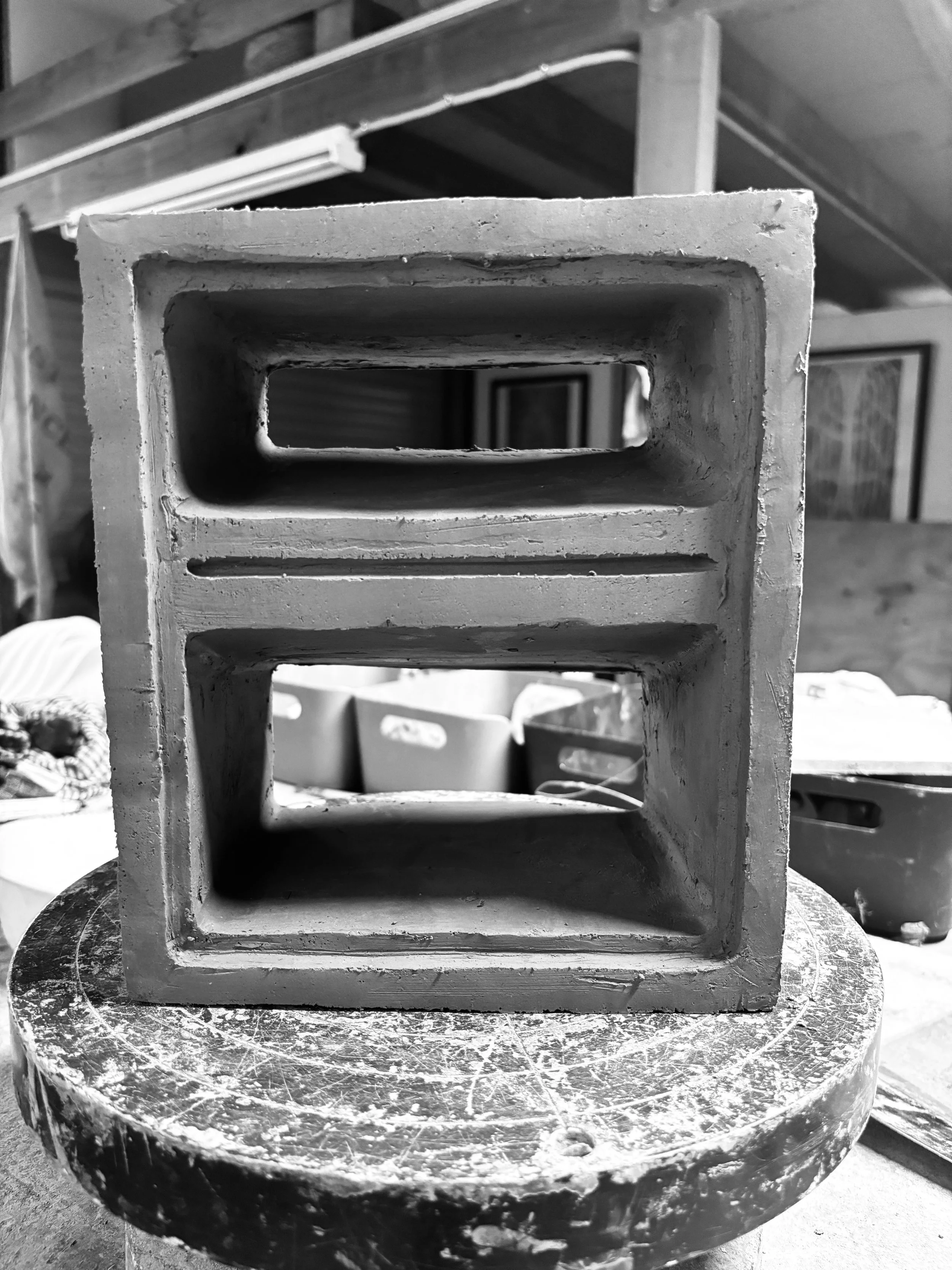 A small concrete block with rectangular cutouts, placed on a round, worn table in a workshop.