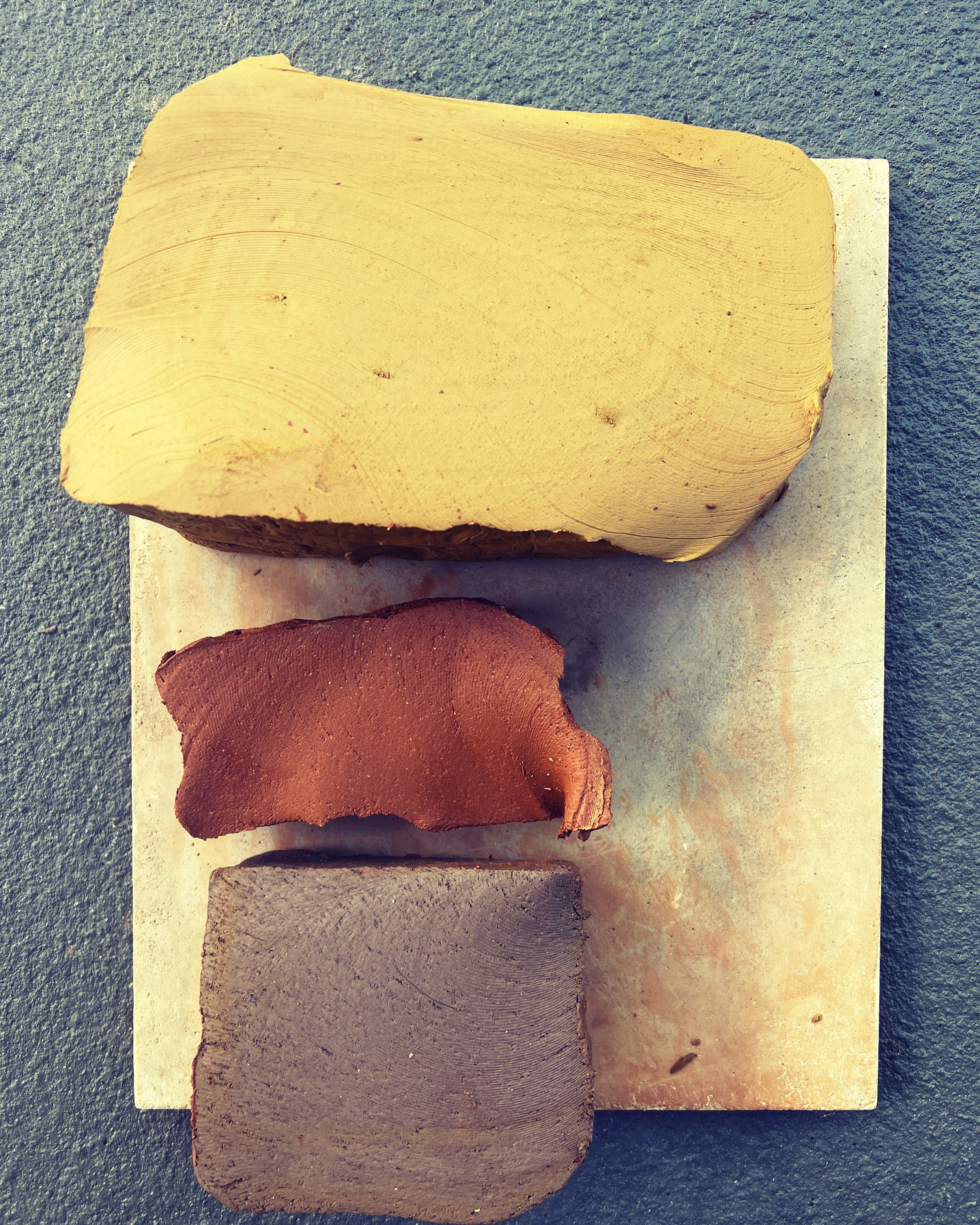 Three different colored clay or ceramic samples placed on a stone surface, arranged vertically.