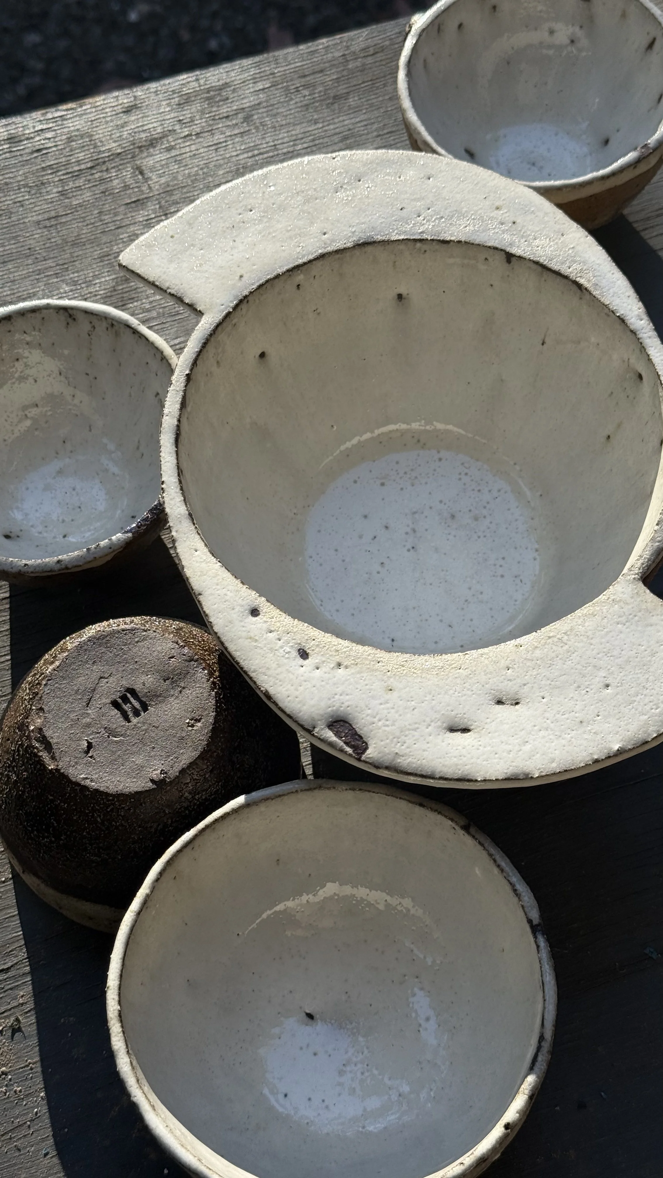 Various ceramic bowls and cups on a wooden surface, some with remnants of water inside.