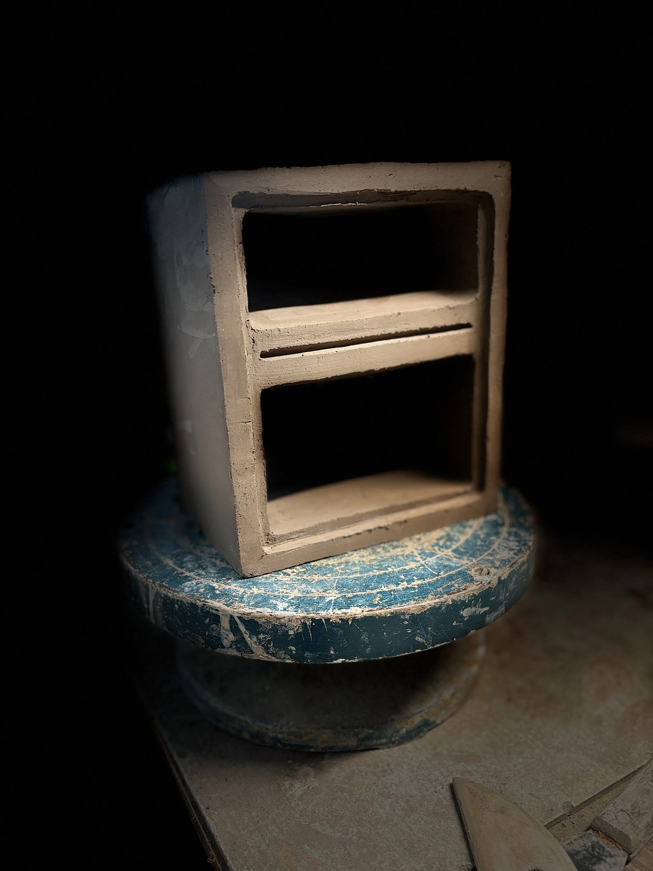 Small unfinished wooden shelf on a blue sanding block with woodworking tools nearby.