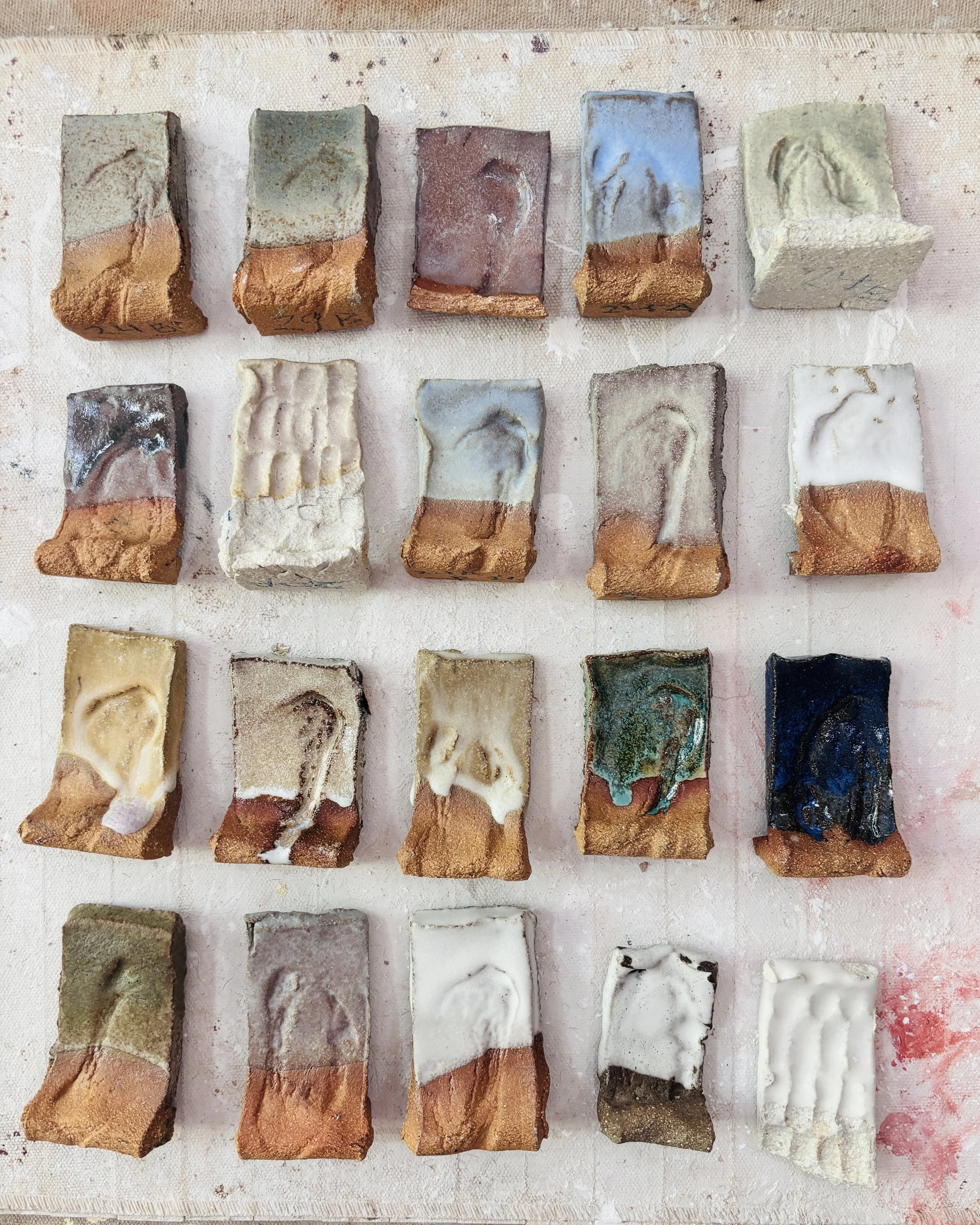 Assorted handmade ceramic tiles arranged in a grid, each with unique glazes and textures.