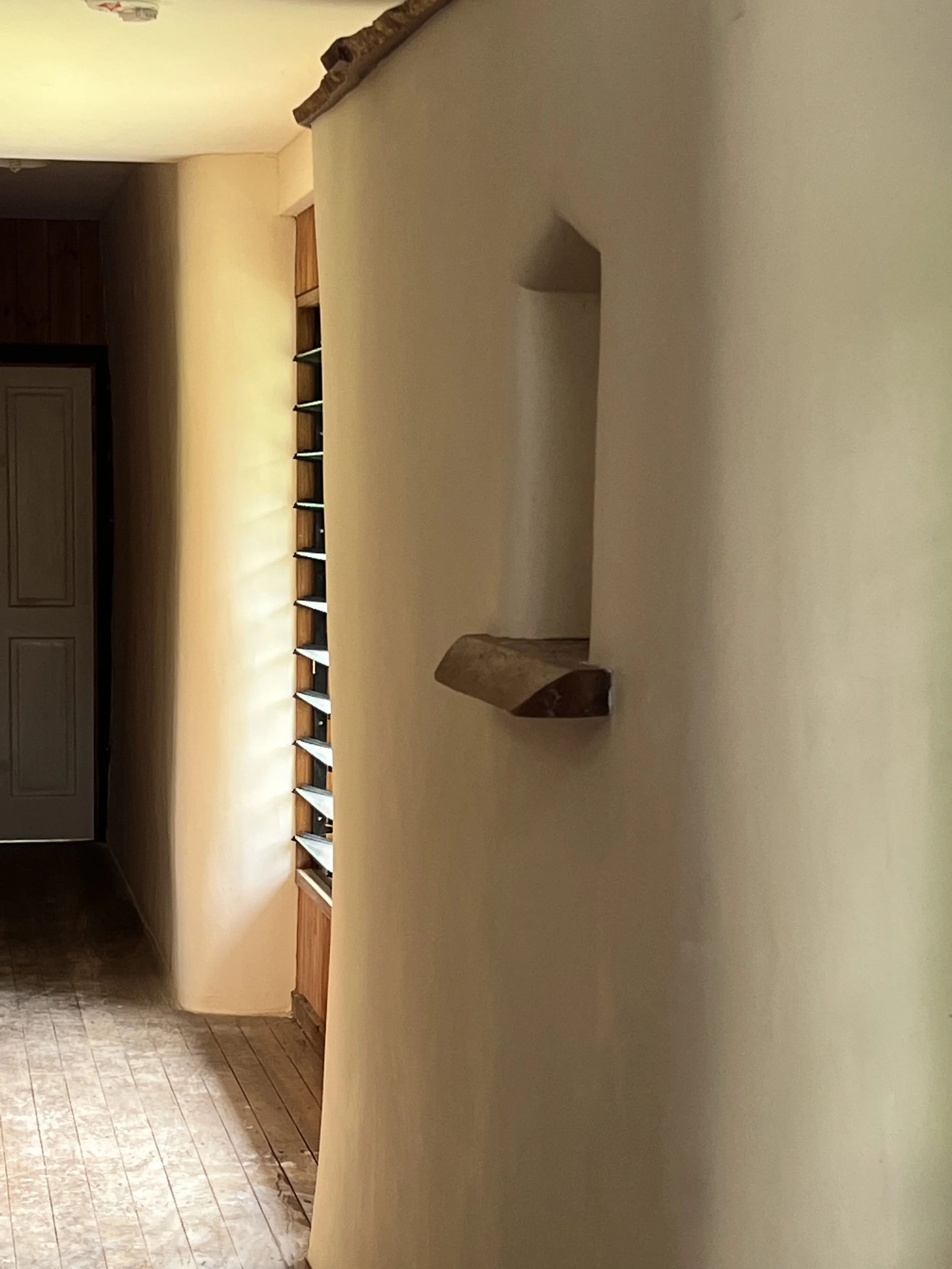 A beige wall with a small built-in shelf or niche attached, made of wood, located in a hallway with a wooden floor.