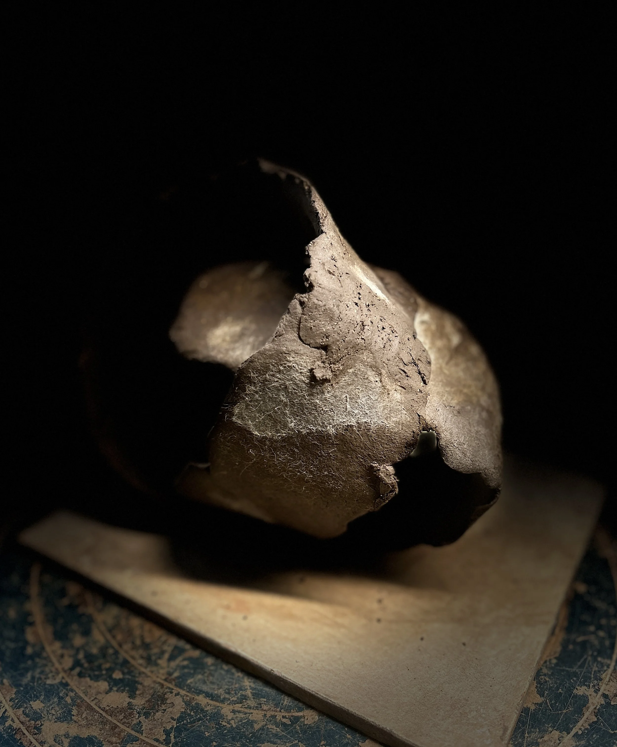 Close-up of a crumpled, dusty, metal object with a rough surface, placed on a piece of paper or cardboard on a dark background.