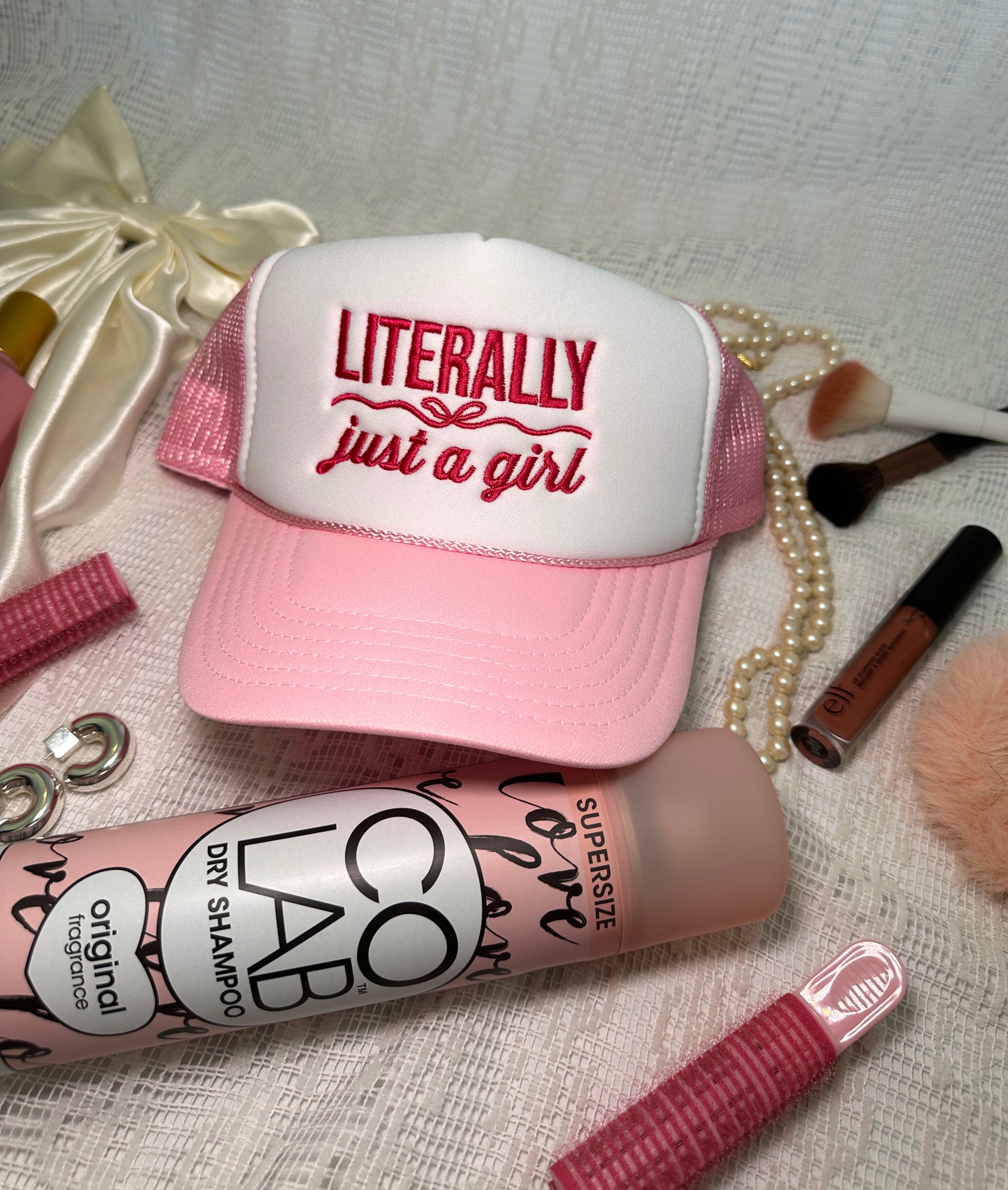 trucker hat photo styled with dry shampoo bottle and other fun pink hair accessories