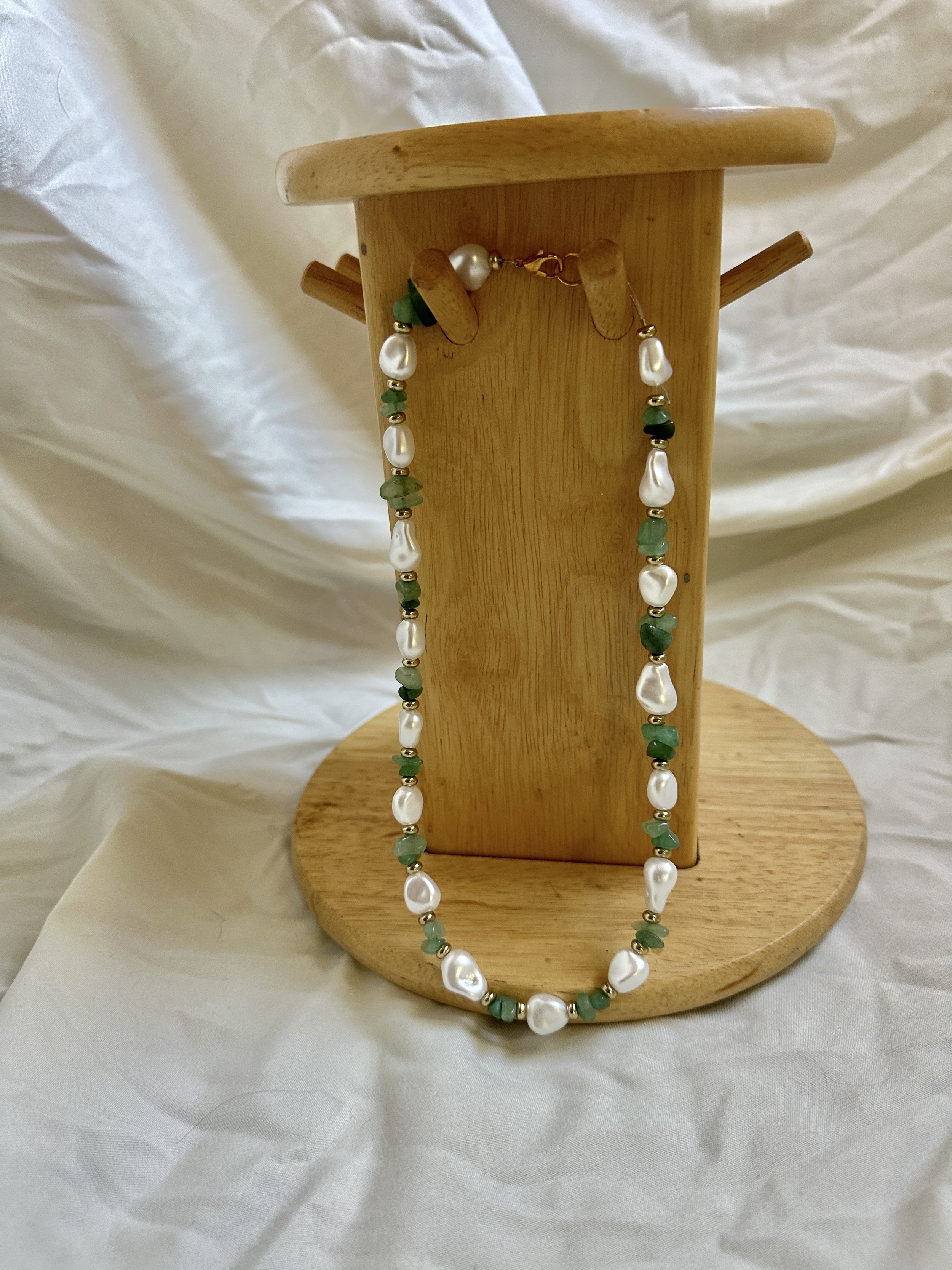 a jade bead, pearl, and gold bead necklace with gold lobster clasp hanging on a wooden jewelry hanging display