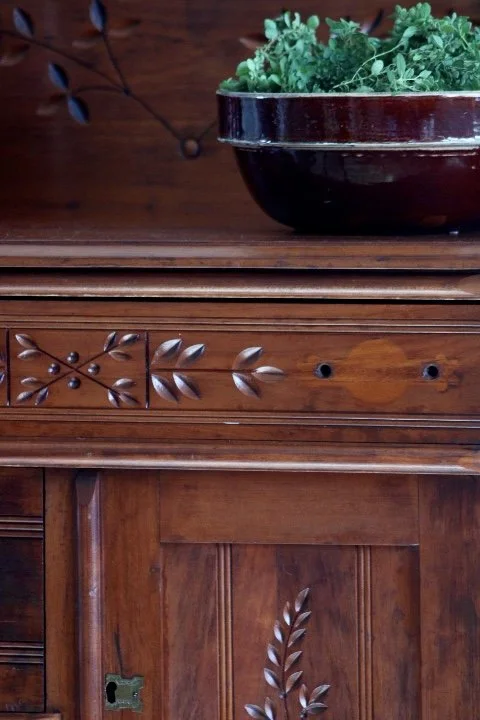 Wooden cabinet with carved floral and leaf patterns, with a black bowl filled with green leafy plants on top.