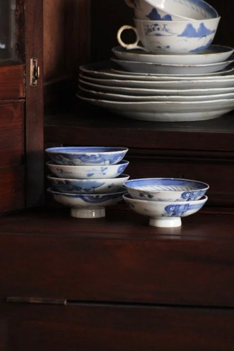 Stacked blue and white porcelain bowls and plates on a wooden shelf.