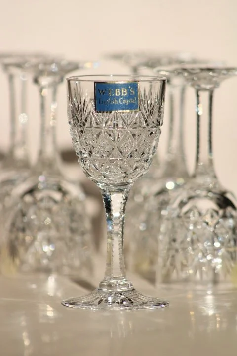 A set of cut glass wine glasses with a close-up of one in the front, labeled 'WEBB'S English Crystal,' with more glasses blurred in the background.