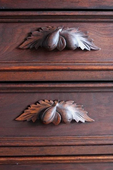 Close-up of two carved wooden drawer handles shaped like acorns with oak leaf details on a dark wooden surface.