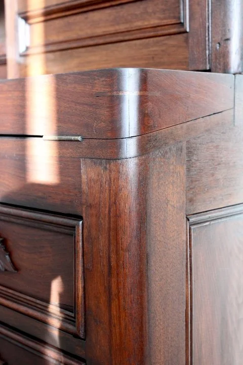 Close-up of a wooden furniture corner with a shiny finish and visible wood grain.