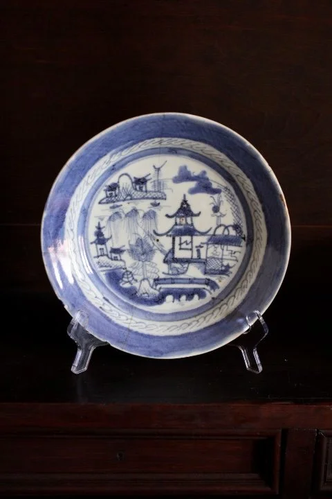 Blue and white ceramic plate with traditional Asian landscape design, displayed on a stand.