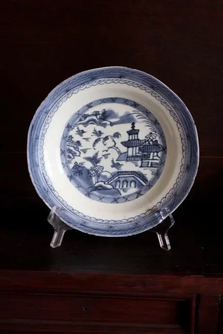 Blue and white decorative porcelain plate with scenic landscape design, displayed on a clear plate stand on a dark wooden surface.