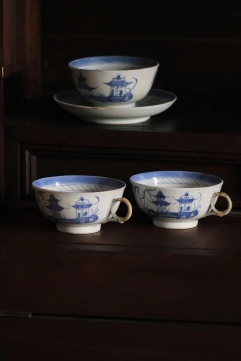 Three blue and white porcelain bowls and matching cups with handles, featuring traditional Asian designs, arranged on a dark wooden surface.