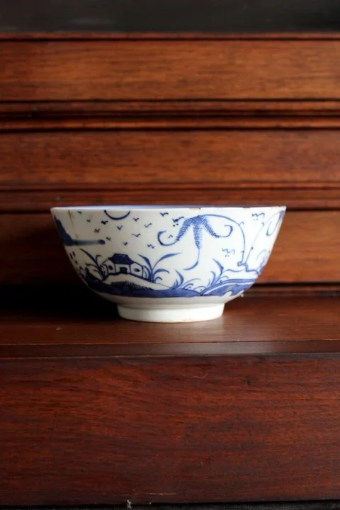 A white and blue porcelain bowl with landscape and dragonfly patterns, placed on a wooden surface against a wooden background.