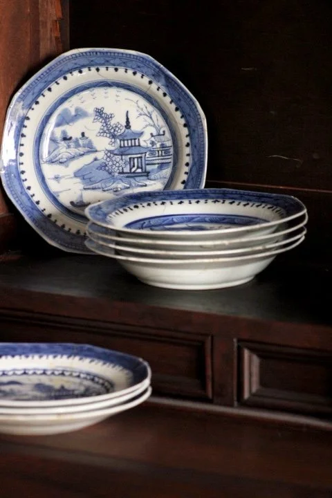 Stack of blue and white decorative plates with scenic design on dark wood surface.