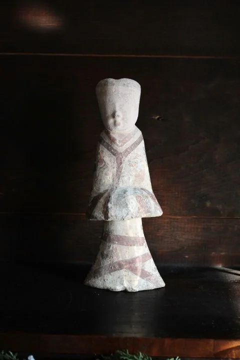 Ancient stone sculpture of a human figure with a simplified, abstract form, featuring a rounded head and a flowing, curving dress.