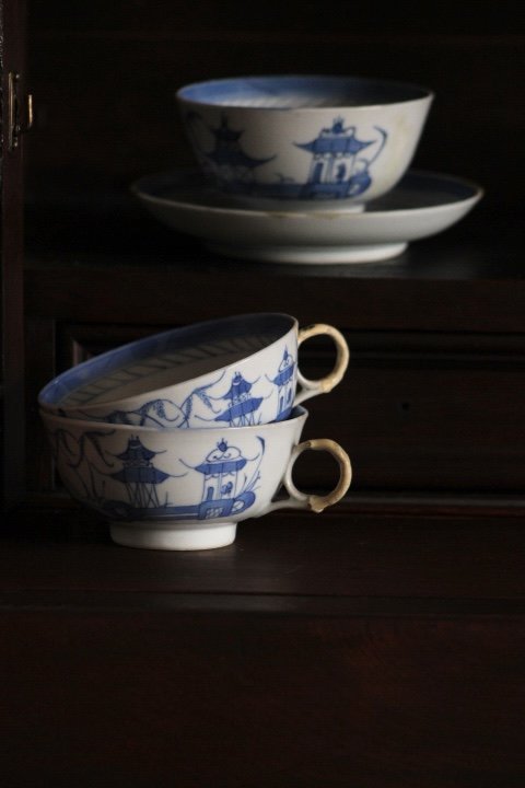 Set of three blue and white porcelain bowls with Asian-inspired designs, stacked with two on a dark wooden surface and one elevated on a plate in the background.