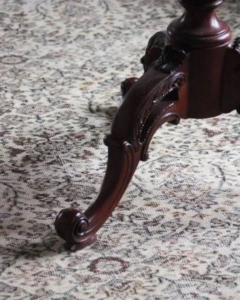 Close-up of the ornate wooden leg of a table on a patterned carpet.