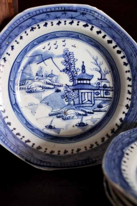 Blue and white porcelain plate with a landscape scene featuring mountains, a river, trees, a pavilion, and flying birds.