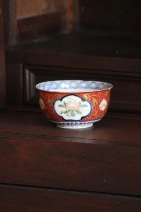 A decorative porcelain bowl with red, blue, and white patterns placed on a dark wooden surface.