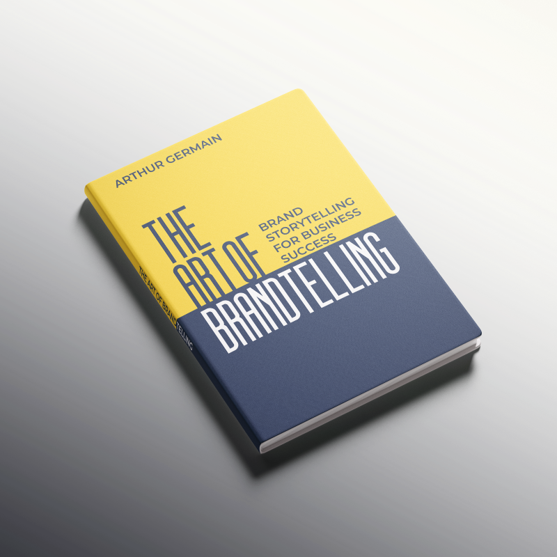 Book titled 'The Art of Brandtelling' by Arthur Germain, with a yellow and dark blue cover, resting on a gradient black to white surface.