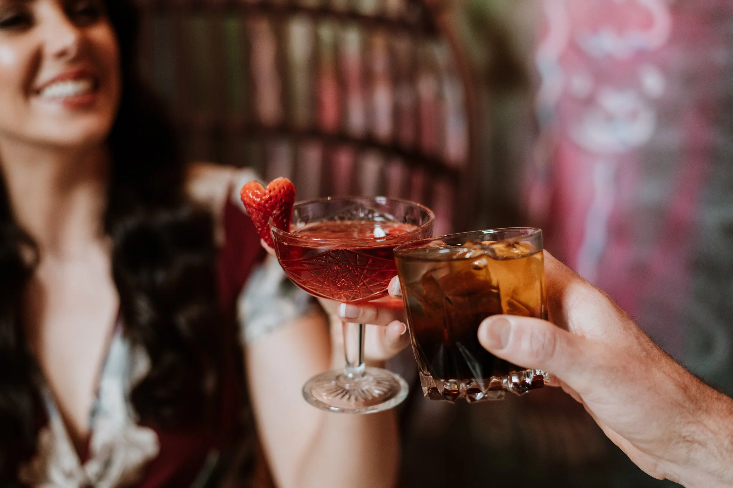 Two women cheers with drinks at a social gathering, with a woman in the background smiling.
