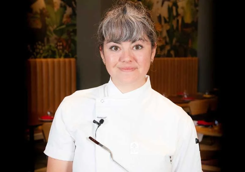 A woman in a white chef's coat standing in a restaurant.