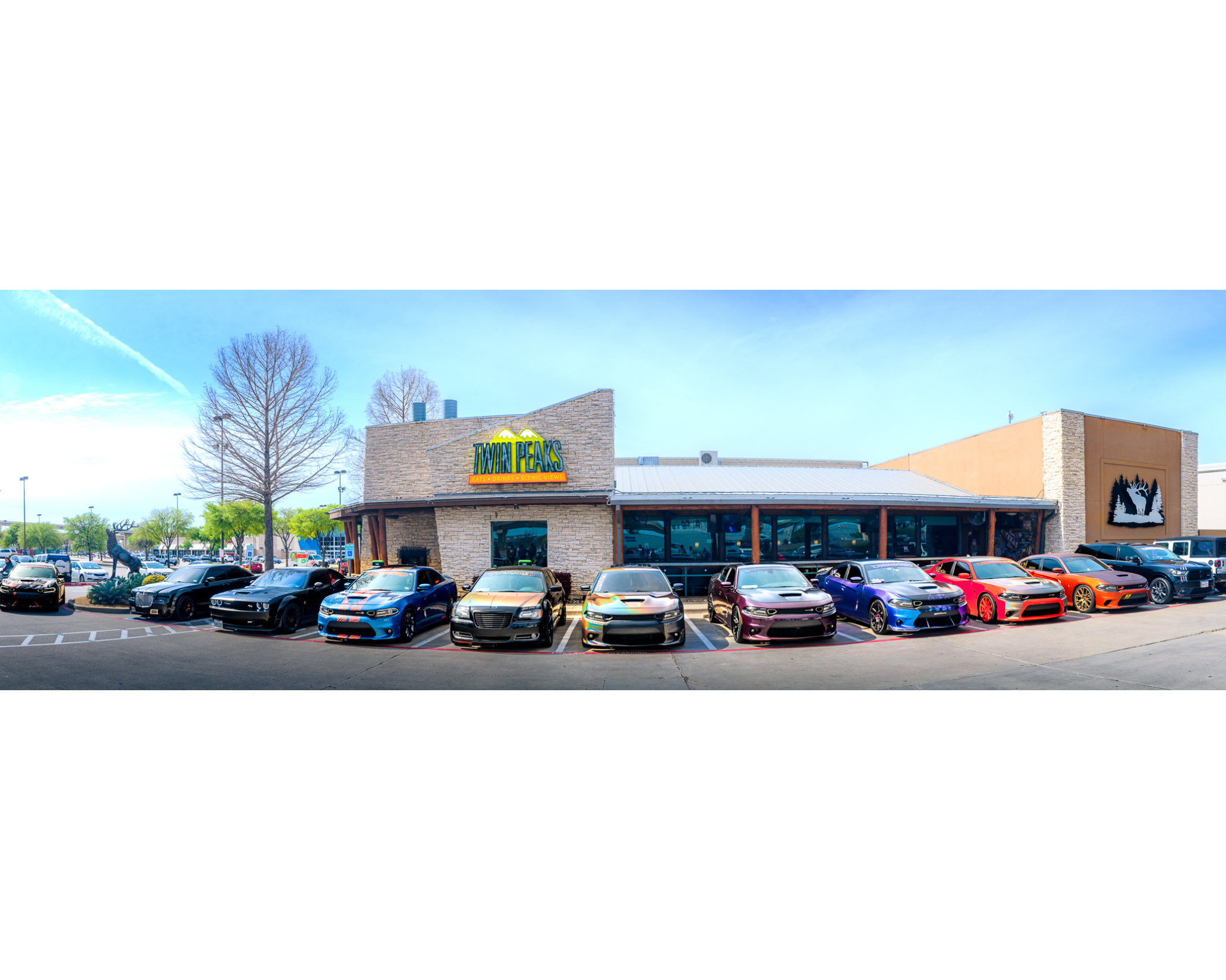 Front view of a restaurant called Twin Peaks with colorful sports cars parked in front on a bright, sunny day.