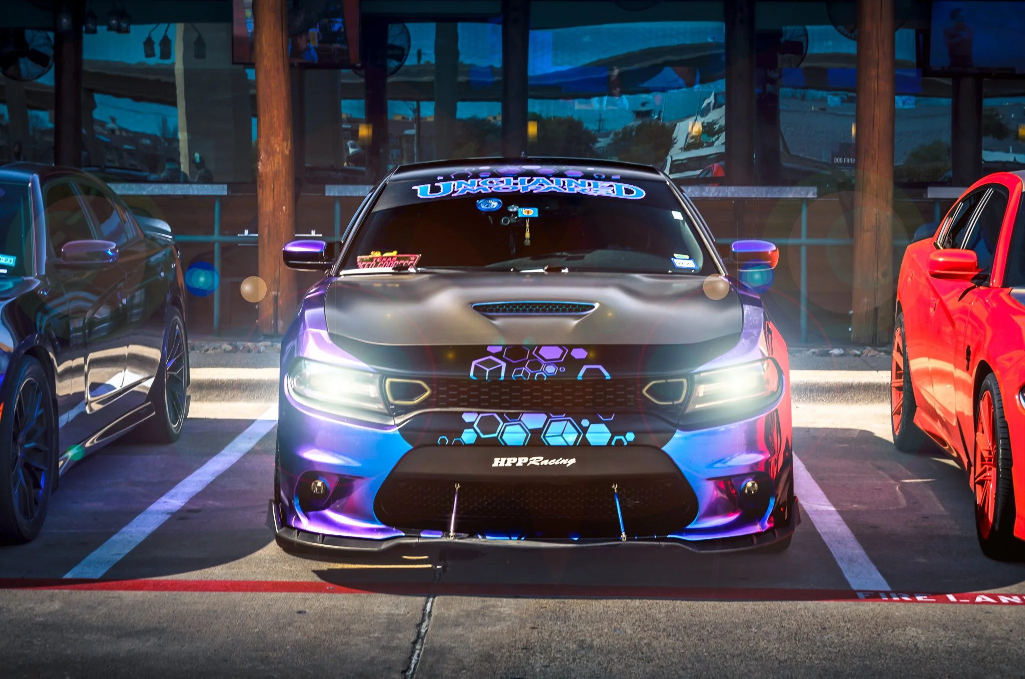 A set of modified race cars parked in a lot, with the central black and purple car displaying glowing hexagonal patterns and decals, including 'HPP Racing' on the front bumper.