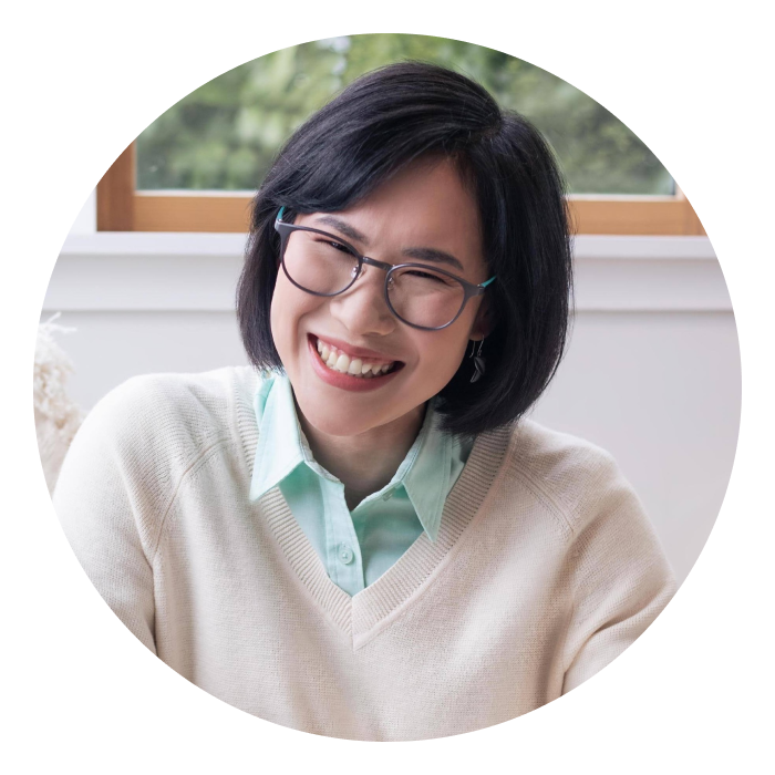 Prae is a middle-aged Thai woman with dark brown eyes and dark hair. She is wearing a white jumper and glasses, and smiling at the camera.