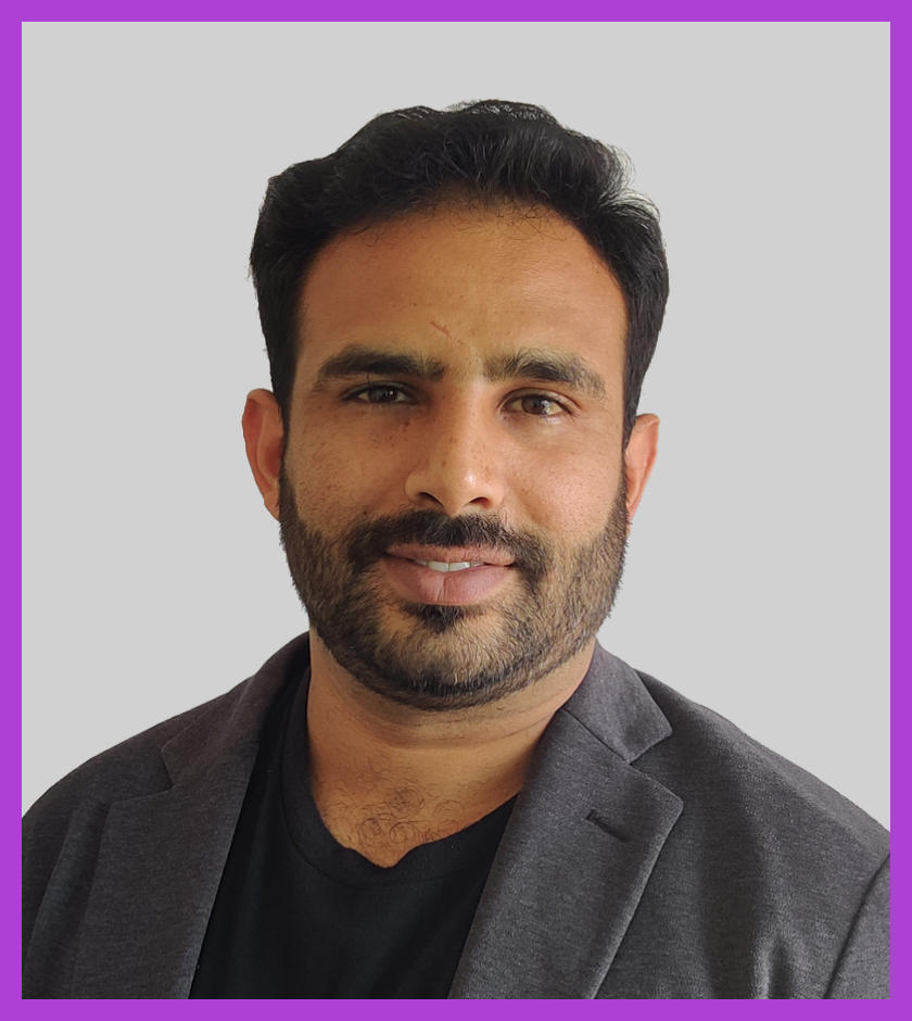 Dipin has dark hair and a beard. He is wearing a black t-shirt and a grey blazer, and smiling at the camera.