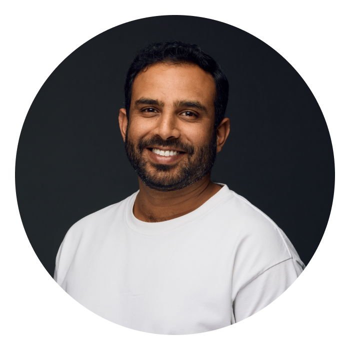 Dipin is a middle-aged Indian male with short dark hair and a beard. He is wearing a white t-shirt and smiling at the camera.