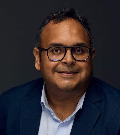 Deep is an Indian male wearing glasses and a navy suit, smiling at the camera.