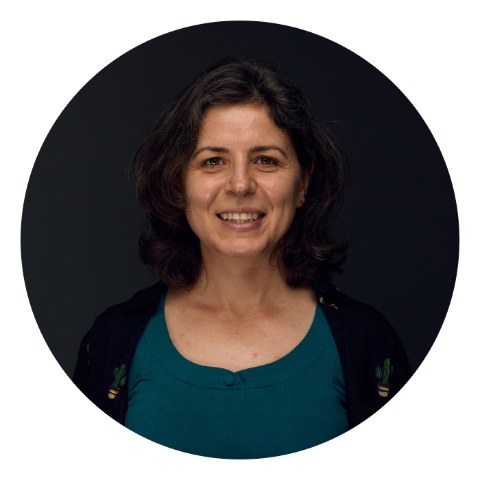 Headshot of Lora - a light skinned woman with light brown hair and wearing a teal top and a black cardigan, smiling at the camera.