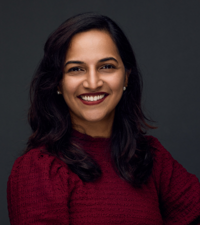 A headshot of Ramya, a middle-aged Indian woman with dark hair, wearing a maroon top and a bright smile on her face.