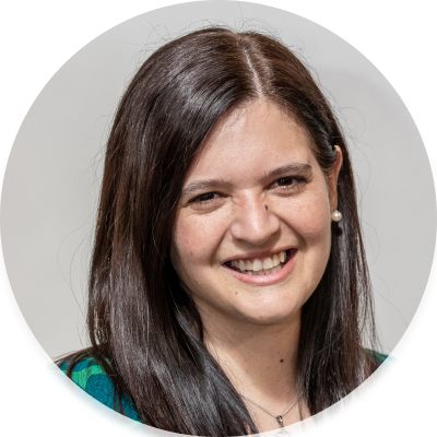 Pauli is a middle aged woman with long dark hair and light skin. Pauli is wearing a green top and smiling at the camera.