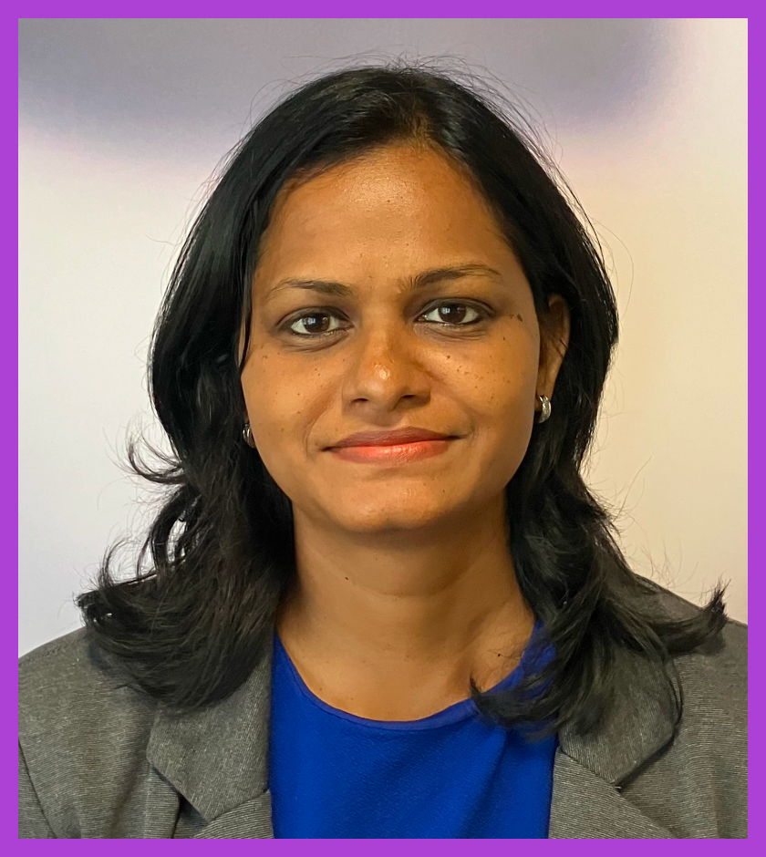Headshot of Surya - a woman with mid length dark hair, wearing a blue top and gray jacket. Surya is slightly smiling at the camera.