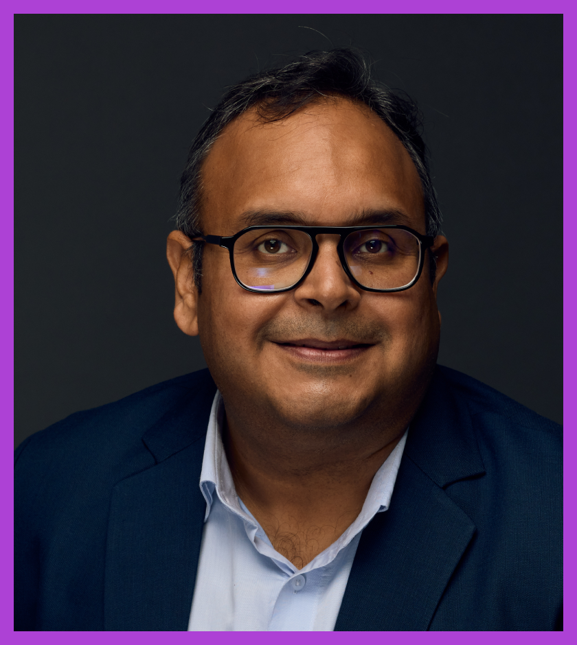 Headshot of Deep - an Indian male wearing glasses and a navy suit, smiling at the camera.