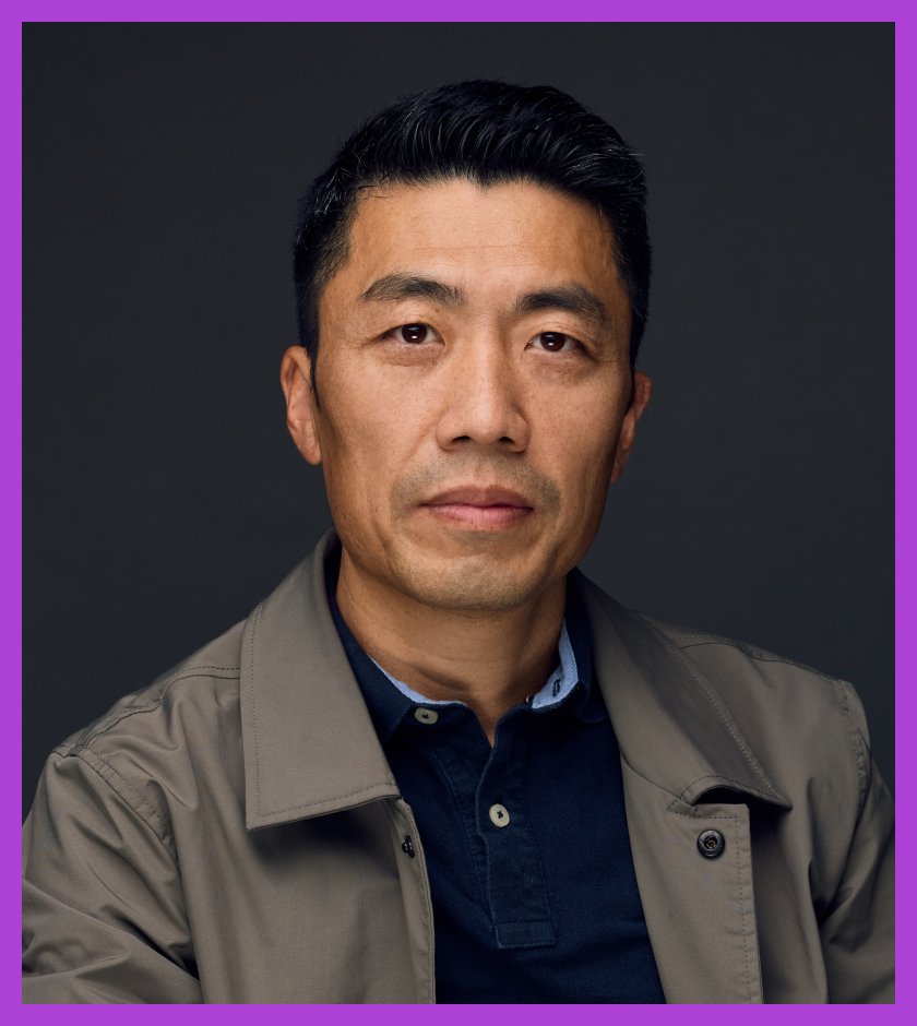 Feilong is a middle-aged Chinese man, wearing a navy blue shirt and smiling at the camera.