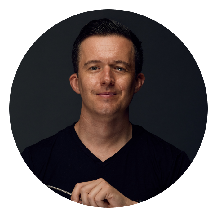 Oli is a Caucasian man with short brown hair, wearing a black t-shirt and smiling at the camera.